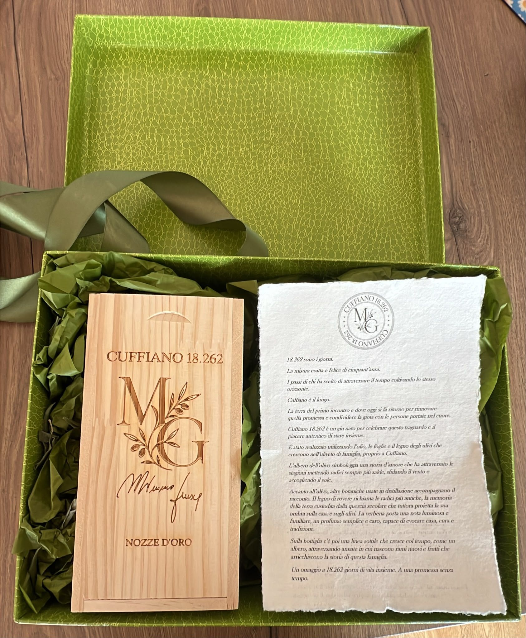 Il cofanetto di legno inciso e la pergamena adagiati in una scatola regalo foderata di verde, con il nastro di raso di lato.